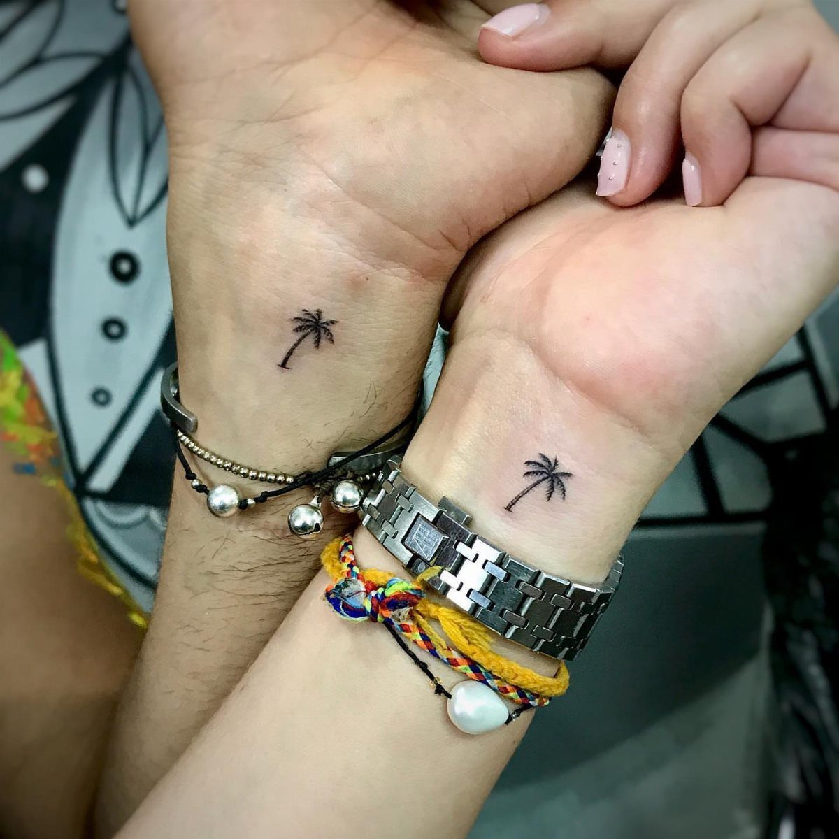 8 Tiny Travel Tattoo Ideas for Your Next Piece of Ink 2 Two wrists side by side, each displaying a tiny black palm tree tattoo and various bracelets.