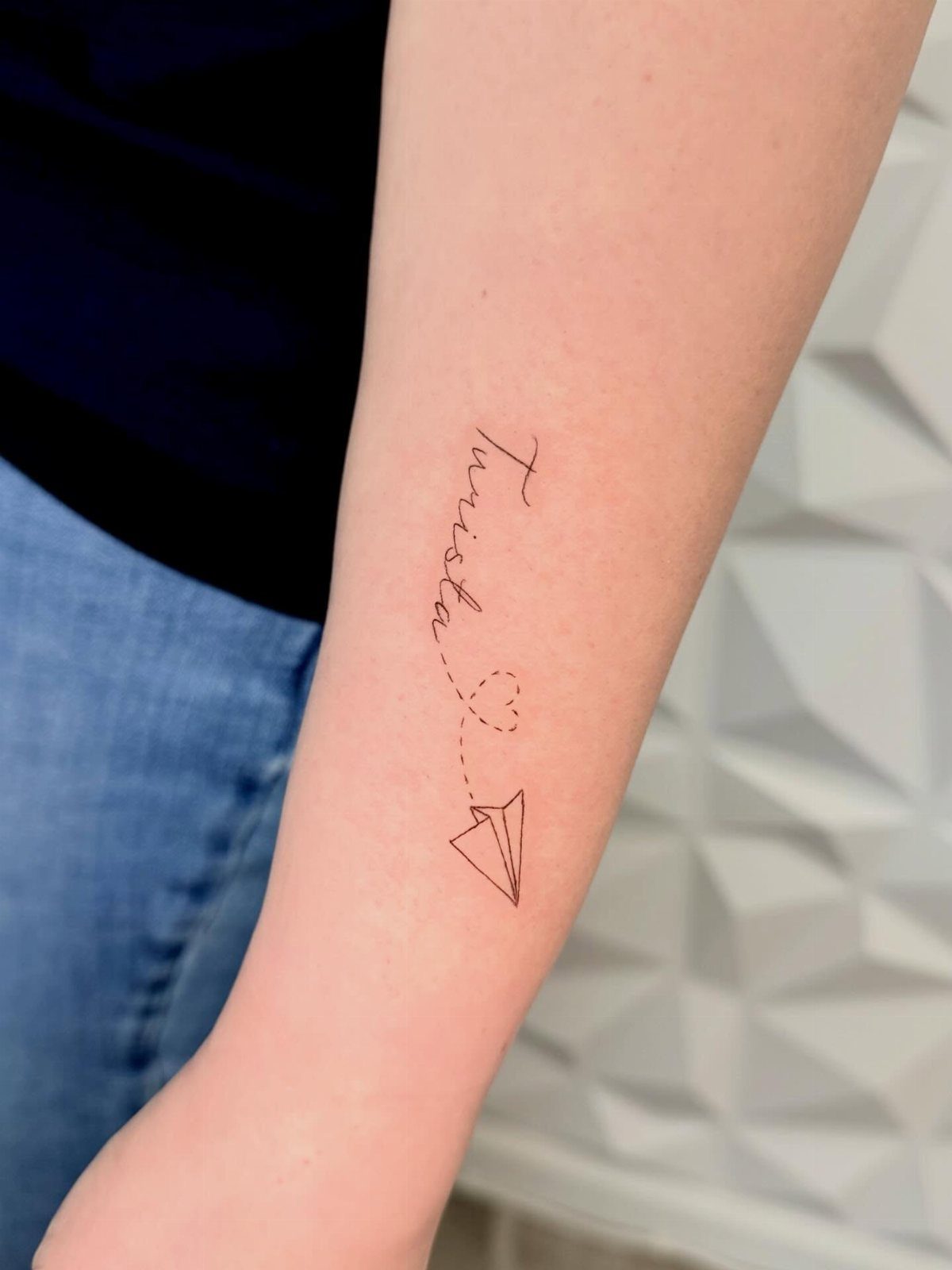 8 Tiny Travel Tattoo Ideas for Your Next Piece of Ink 4 A minimalist black ink tattoo of a paper plane and a heart on a forearm.