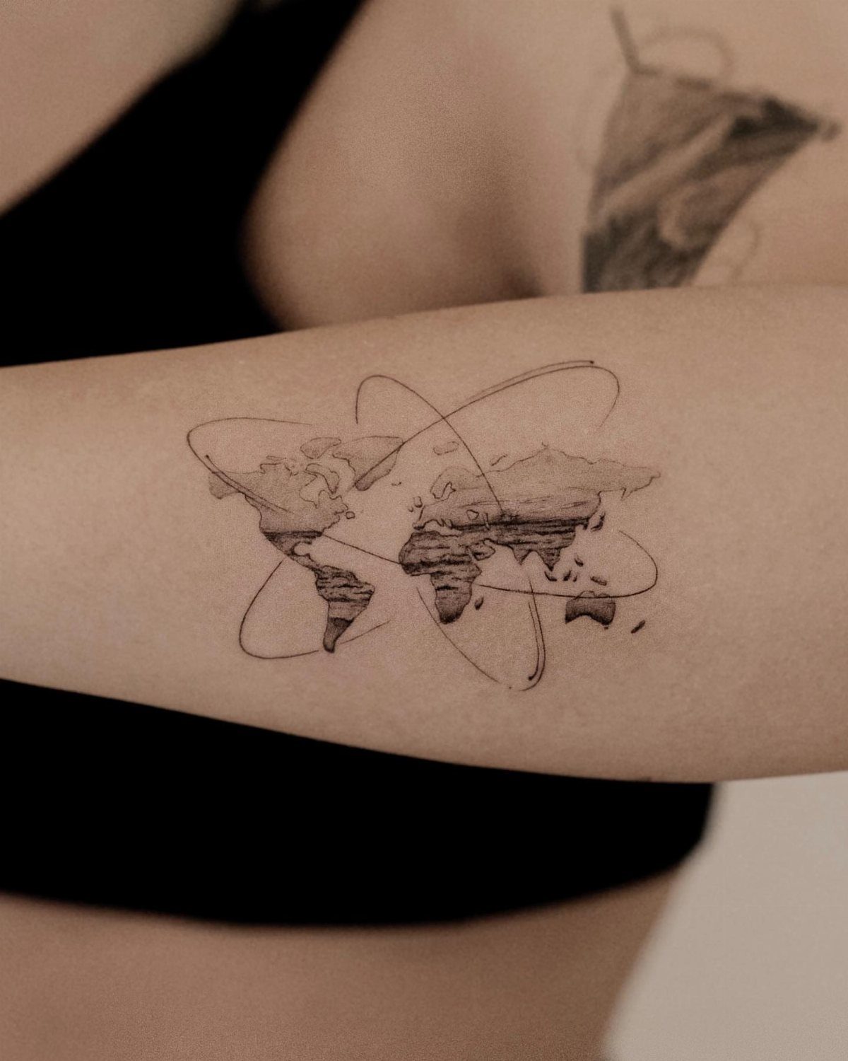 8 Tiny Travel Tattoo Ideas for Your Next Piece of Ink 3 A small black ink world map tattoo with orbital rings on a person's forearm.