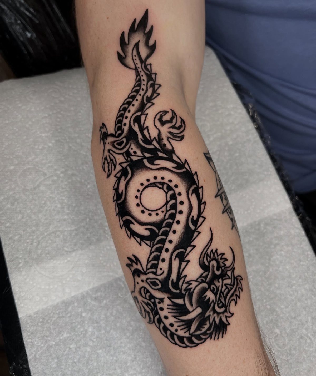 Traditional Dragon Tattoo: 9 Bold Designs That Carry Real Weight 3 A black and grey coiled dragon tattoo on a person's forearm with bold outlines.