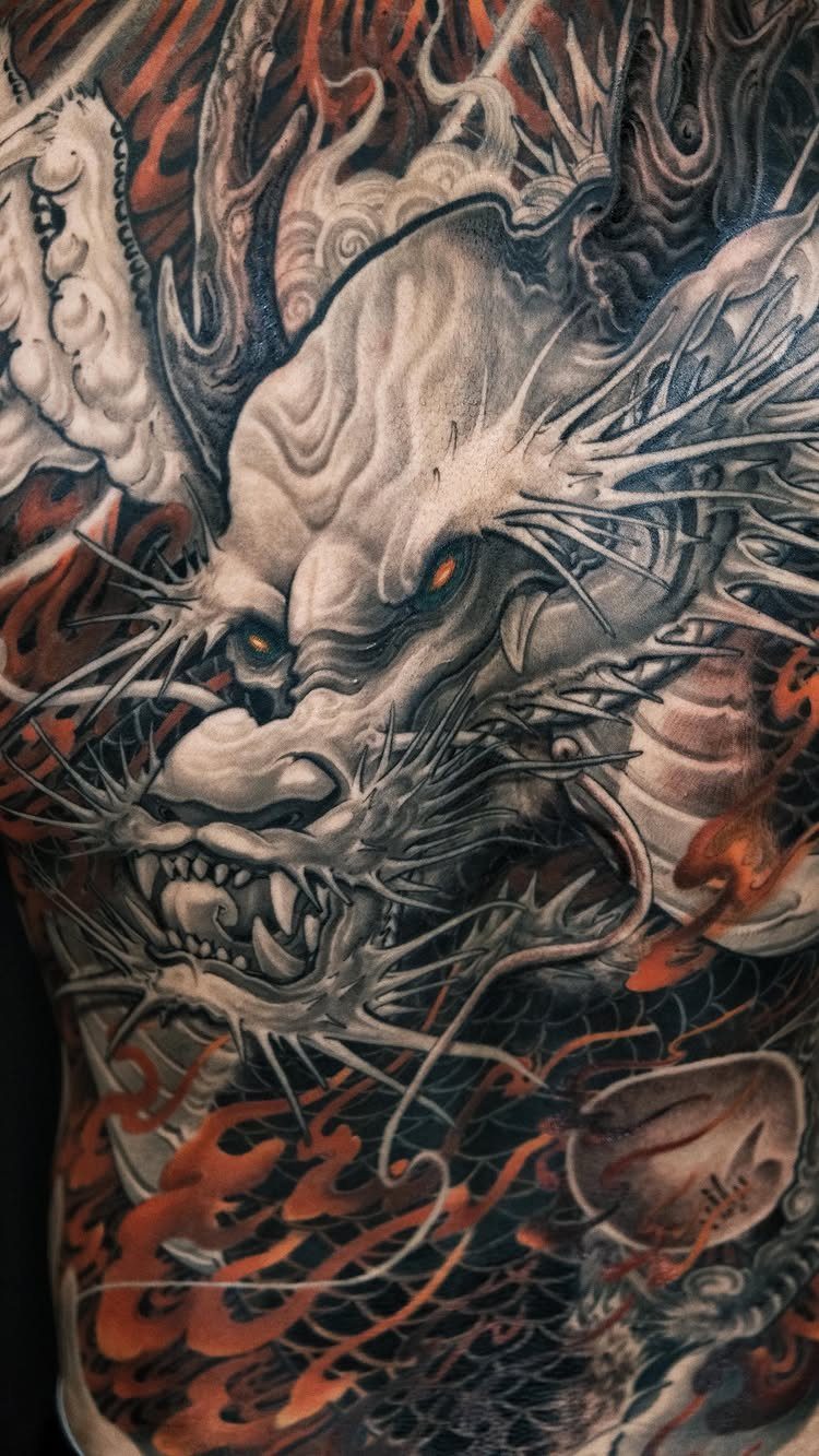 Traditional Dragon Tattoo: 9 Bold Designs That Carry Real Weight 4 A large, intricate dragon tattoo with white and orange details covering a person's back.