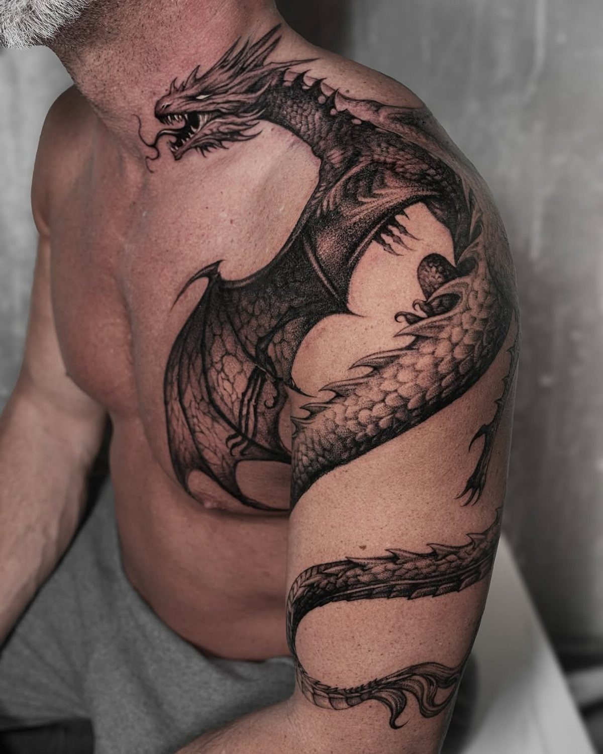 Traditional Dragon Tattoo: 9 Bold Designs That Carry Real Weight 5 A large black and grey dragon tattoo covering a man's chest and shoulder.