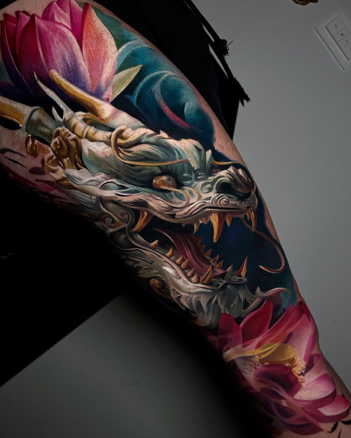 Traditional Dragon Tattoo: 9 Bold Designs That Carry Real Weight 8 A detailed dragon tattoo with pink lotus flowers on a person's leg.