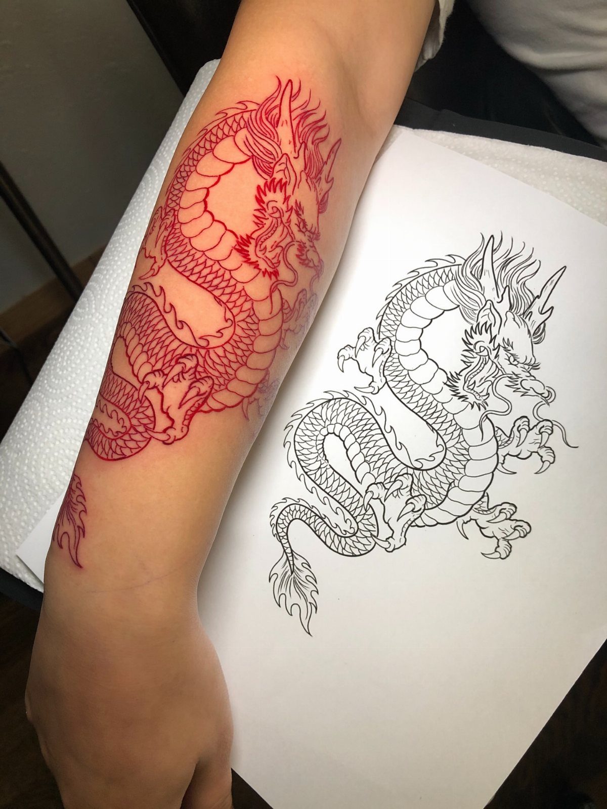 Traditional Dragon Tattoo: 9 Bold Designs That Carry Real Weight 6 A red dragon tattoo on a person's forearm next to its line art drawing.