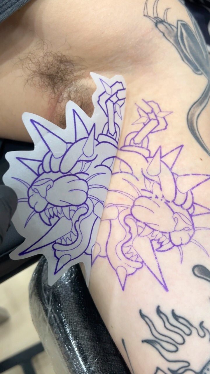 A purple lion head tattoo stencil being transferred onto human skin using translucent paper.