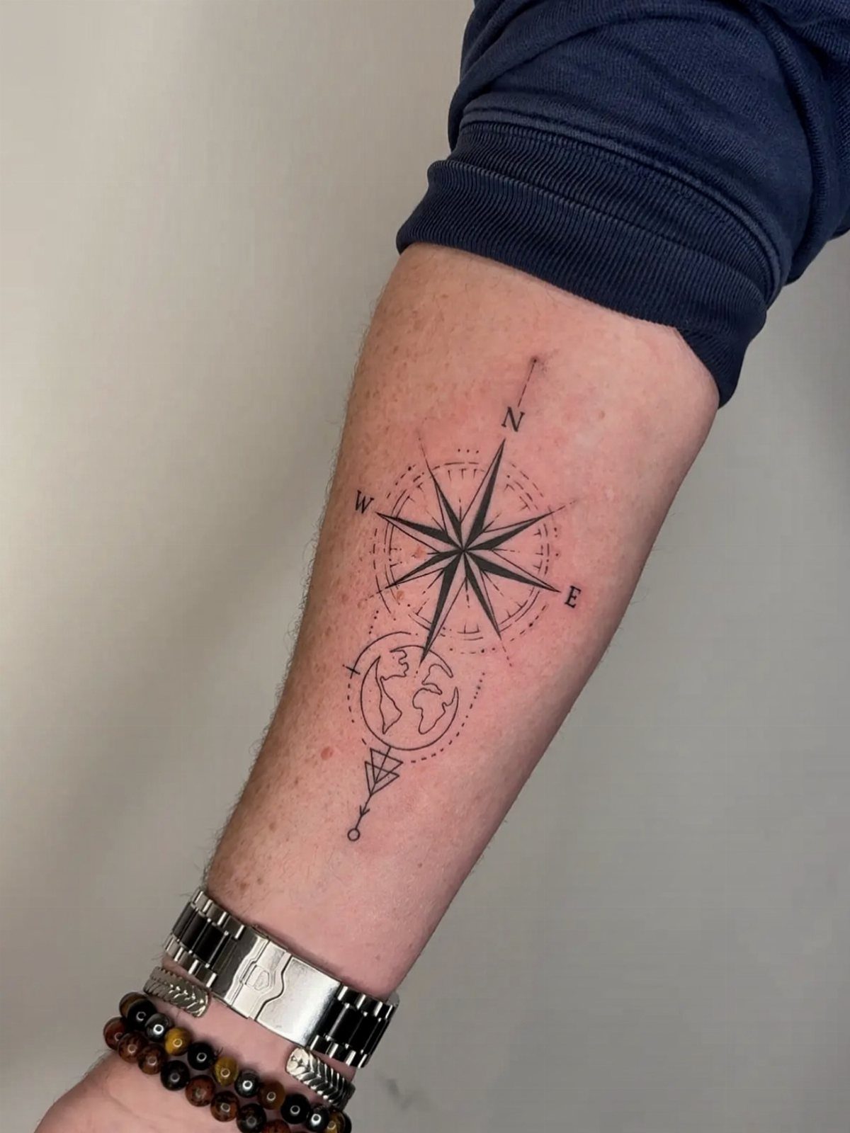 A black ink tattoo of a compass rose and a globe on a person's forearm.