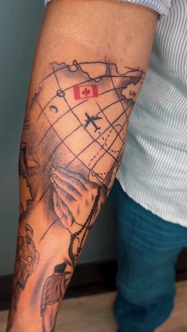 A detailed arm tattoo depicting a world map with a small Canadian flag and an airplane.