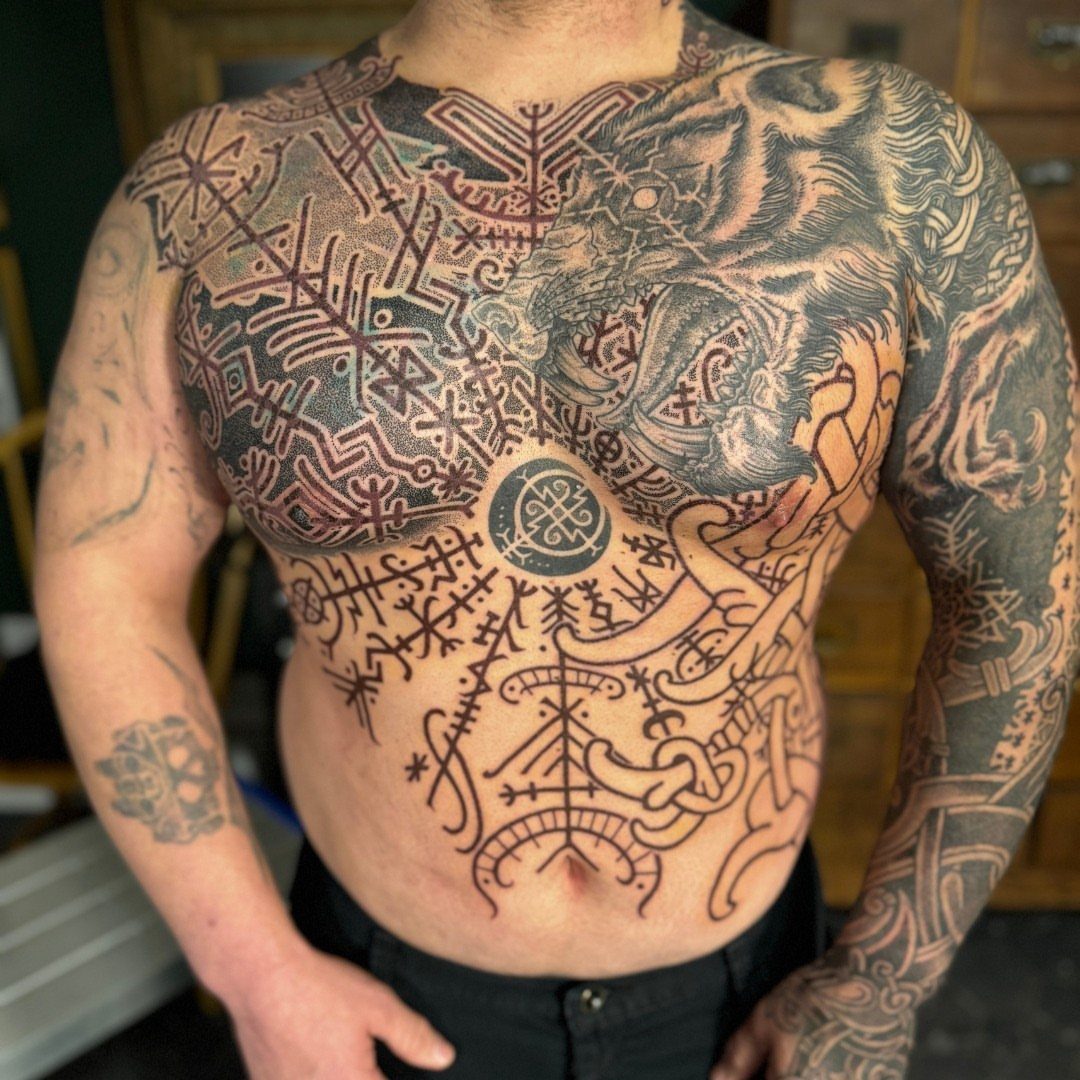 Man with extensive black ink tattoos covering his chest, stomach, and arms in Norse styles.