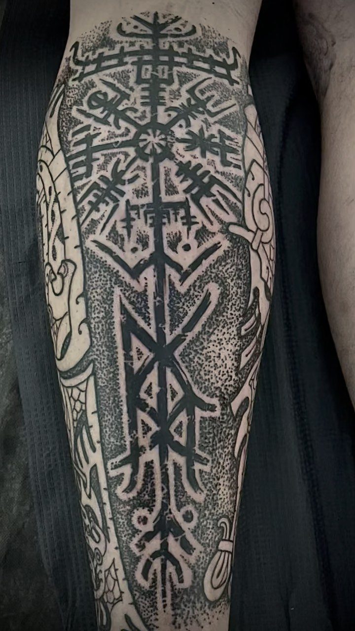A large black ink Viking rune tattoo with geometric patterns on a person's leg.