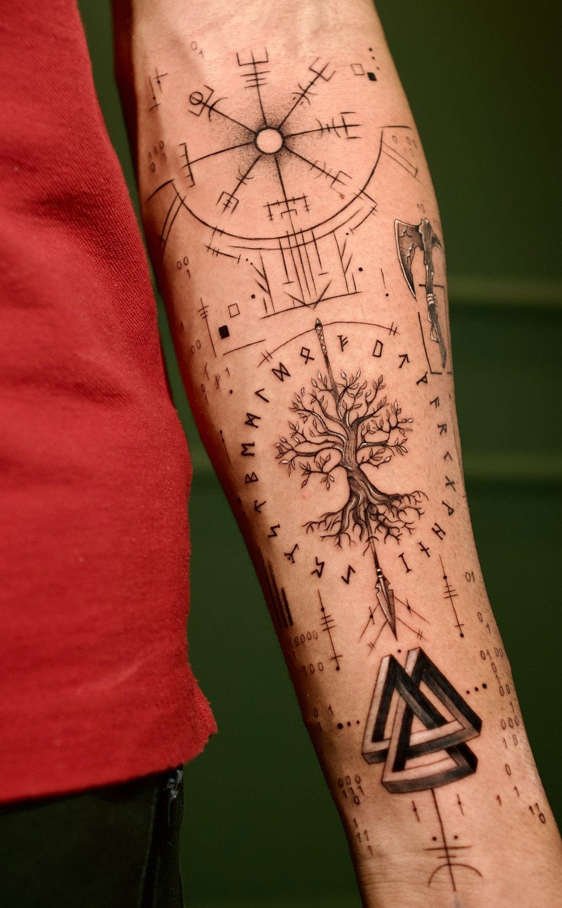 A person's forearm covered in various black ink Viking rune and Norse mythology tattoos.