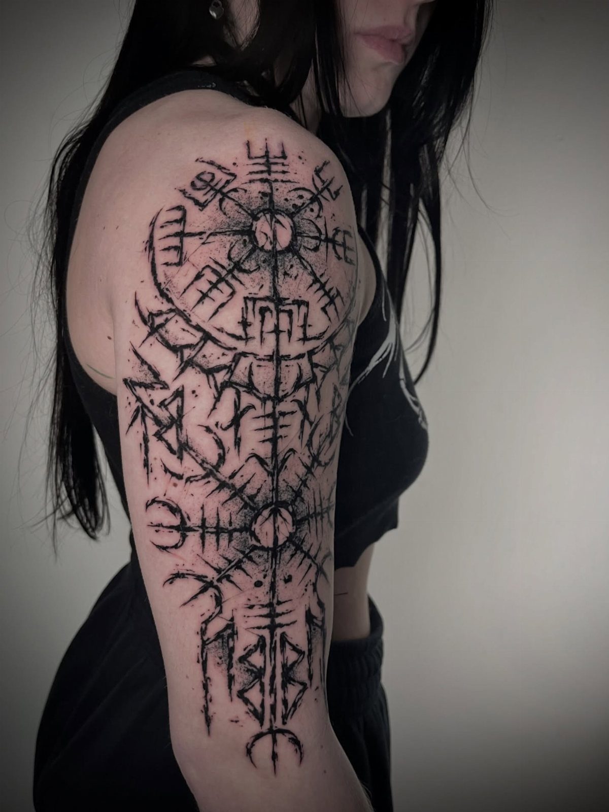 A large black ink Viking rune tattoo covering a person's upper arm and shoulder.
