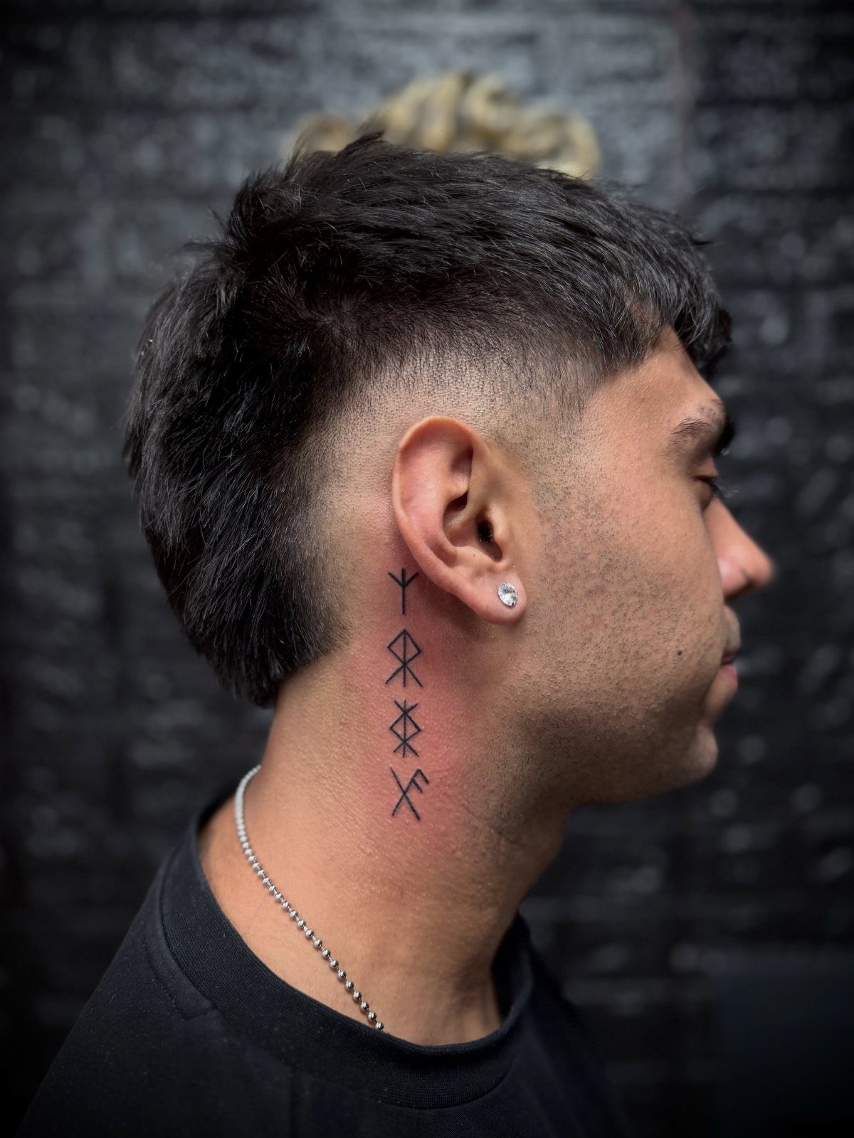A man's profile showing a vertical line of four black Viking rune tattoos on his neck.