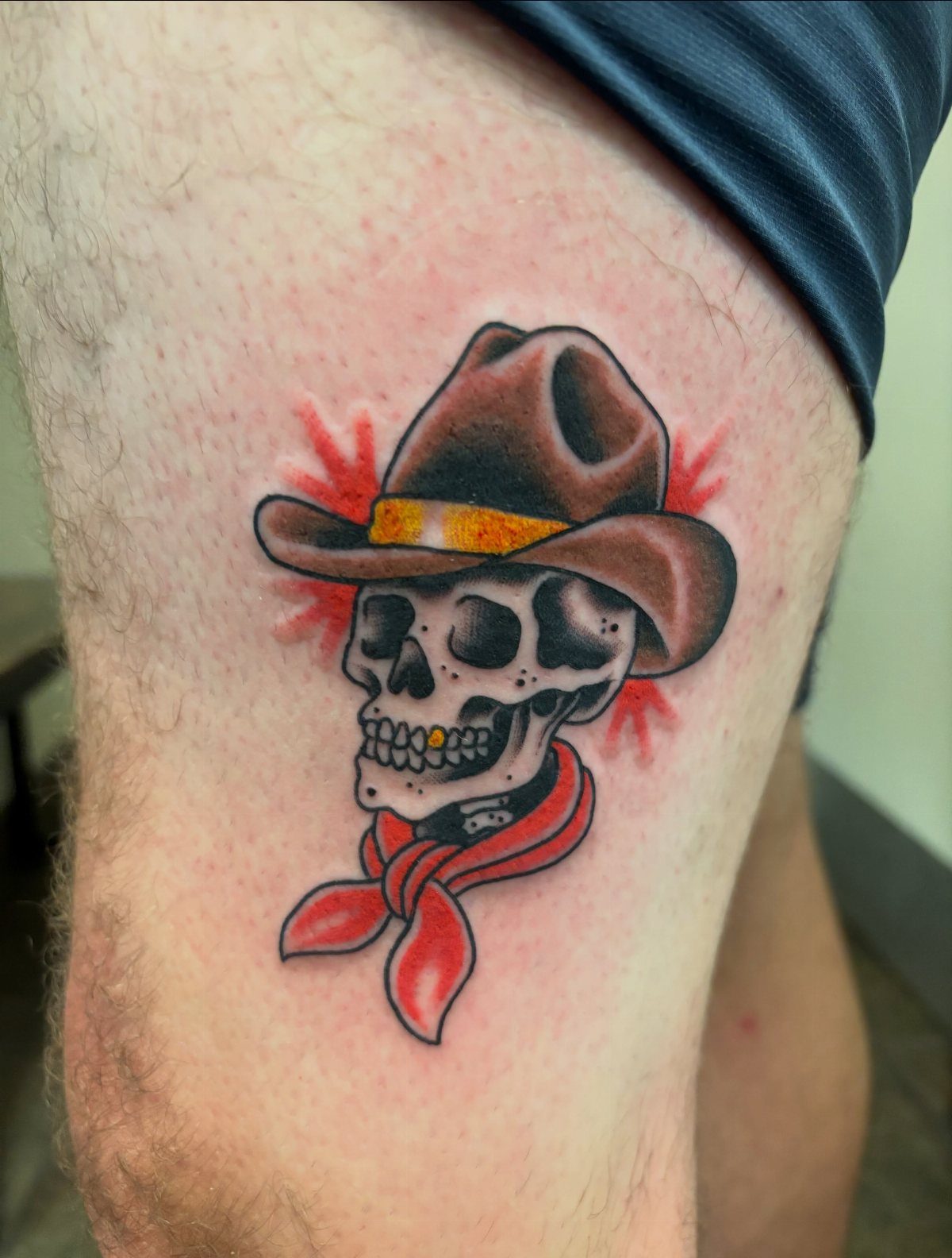 A traditional tattoo of a skull wearing a cowboy hat and a red bandana on a person's leg.