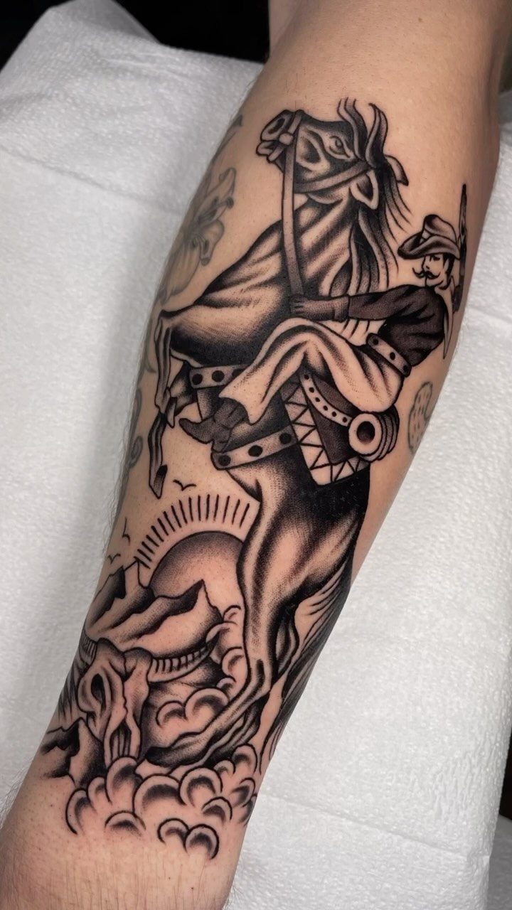 Black and grey traditional tattoo of a cowboy riding a bucking horse over a desert landscape.
