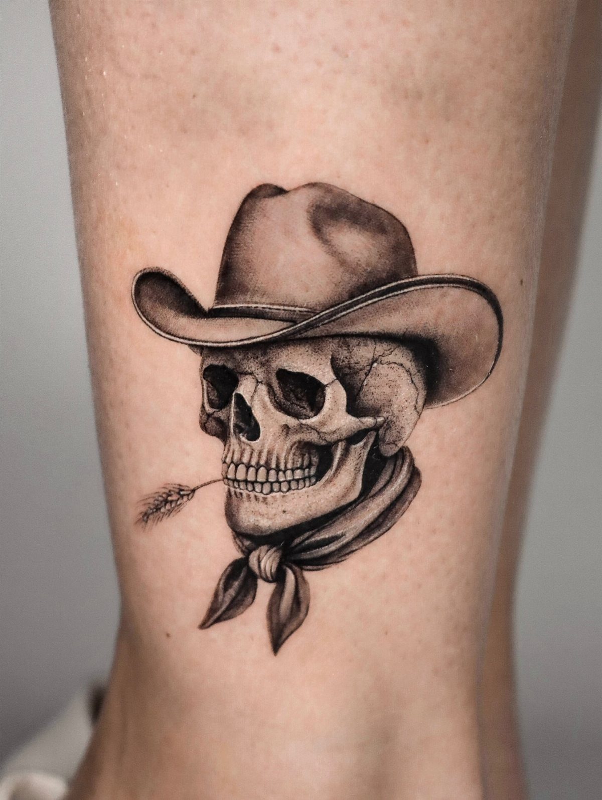 A black and grey tattoo of a skull wearing a cowboy hat and bandana on skin.