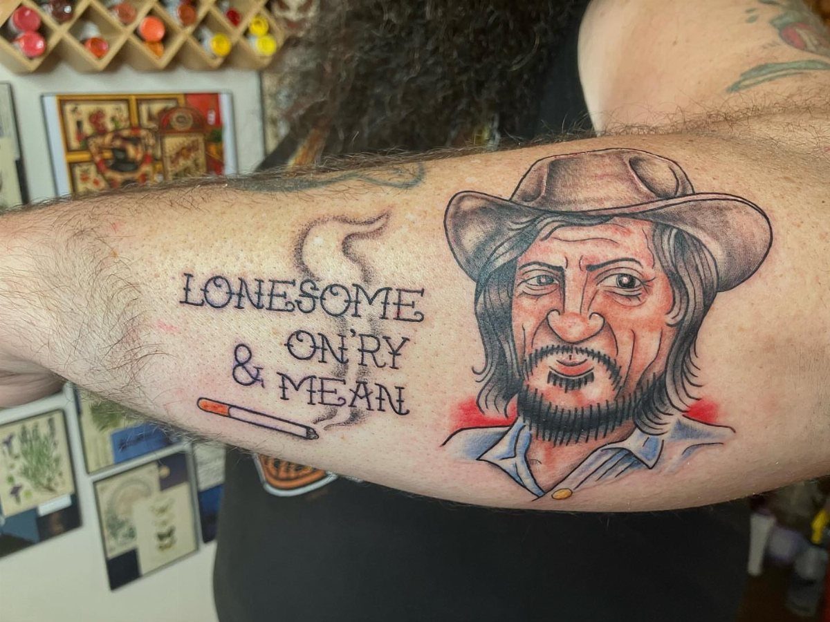A tattoo on an arm depicting a man in a wide-brimmed hat and text.