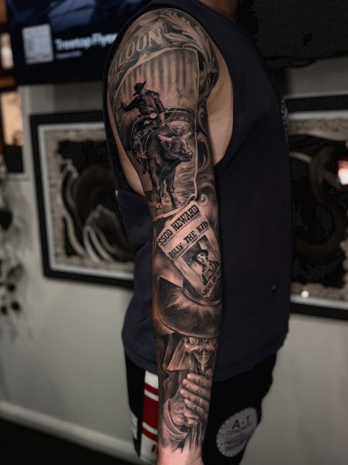 A large black and grey sleeve tattoo on an arm featuring a cowboy riding a bull.