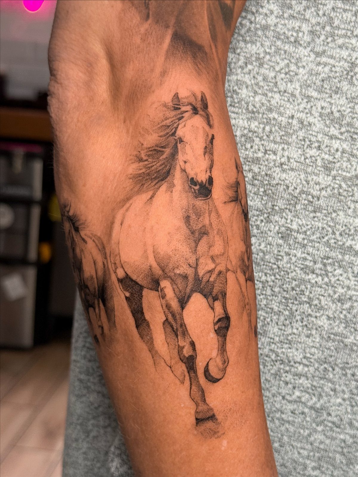 A fine line tattoo of galloping horses on a person's forearm.