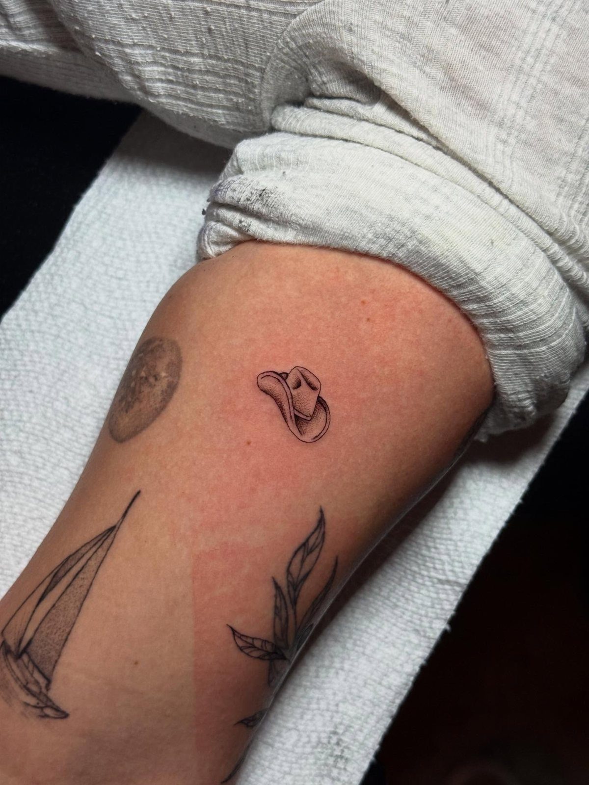 A small fine line cowboy hat tattoo on a person's arm skin.