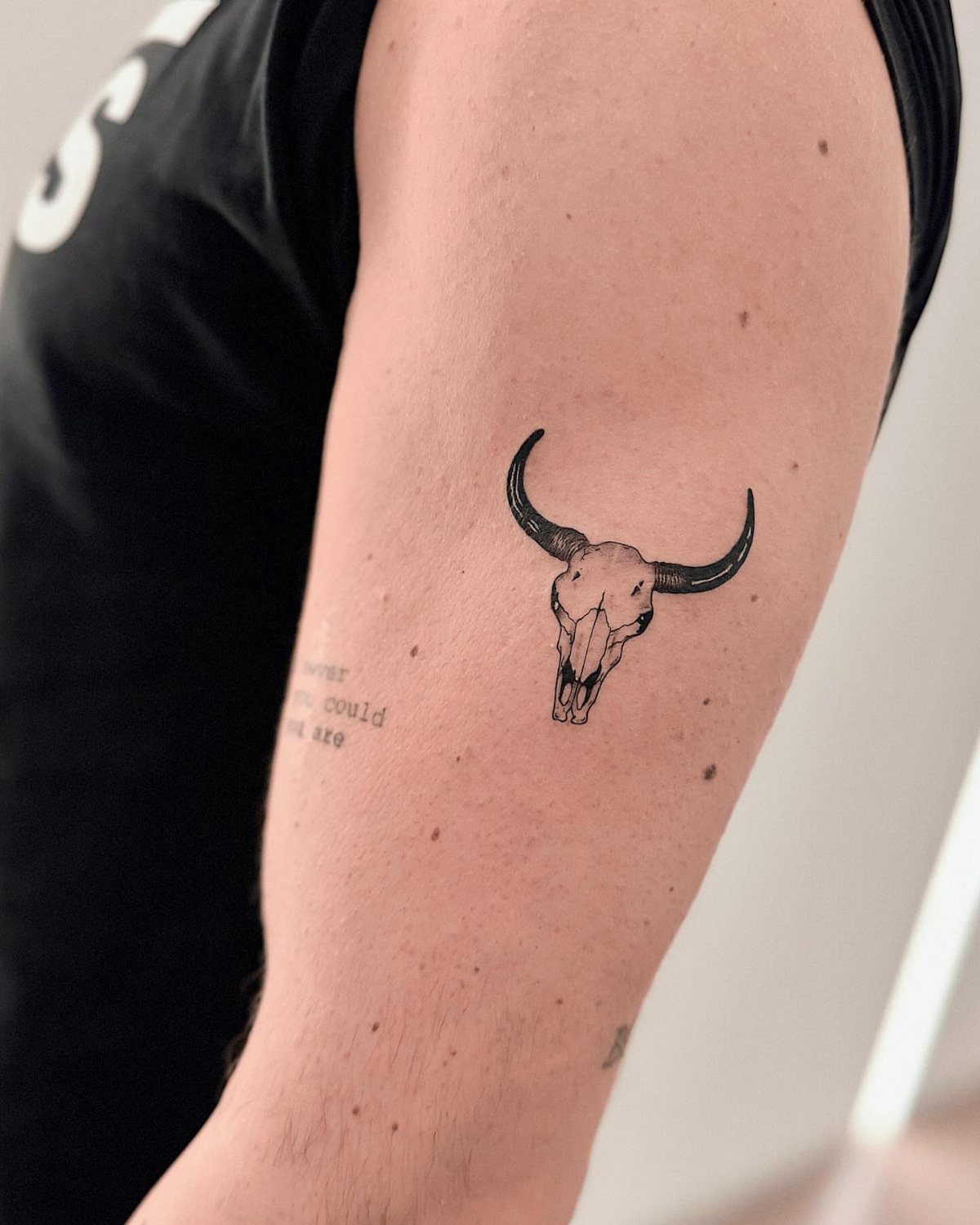 A fine line black ink steer skull tattoo on a person's upper arm.