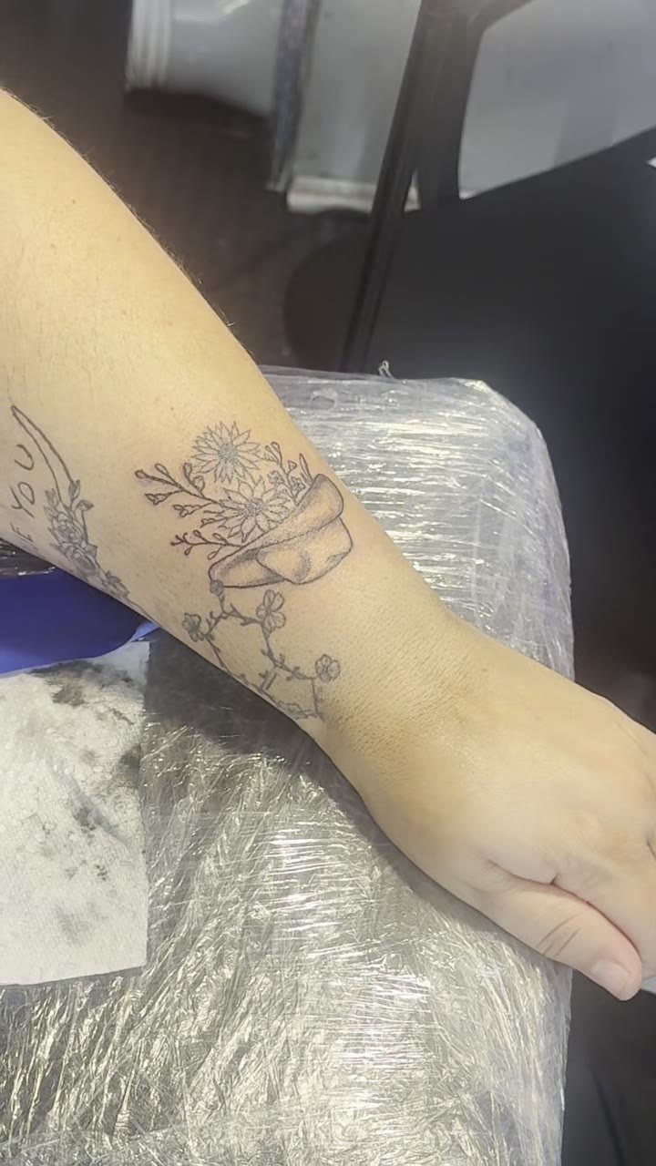 A black ink tattoo of a cowboy hat and wildflowers on a person's forearm.