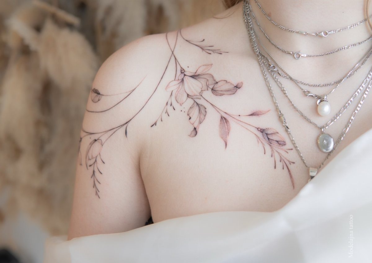 Fine line floral tattoo flowing across a person's shoulder and collarbone area.