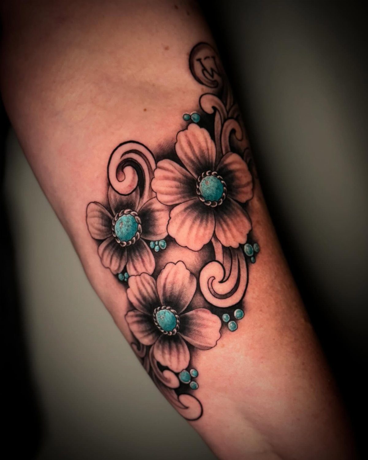 Floral tattoo with black shading and turquoise gemstone accents on a person's arm.