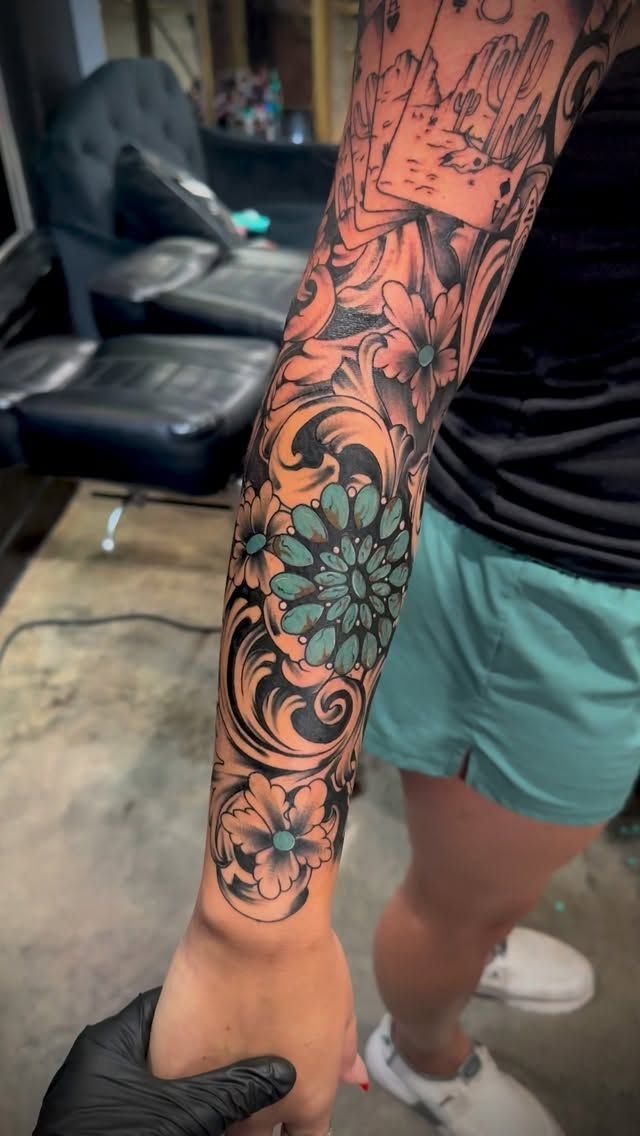 A detailed black and grey floral tattoo sleeve with turquoise accents on a person's arm.
